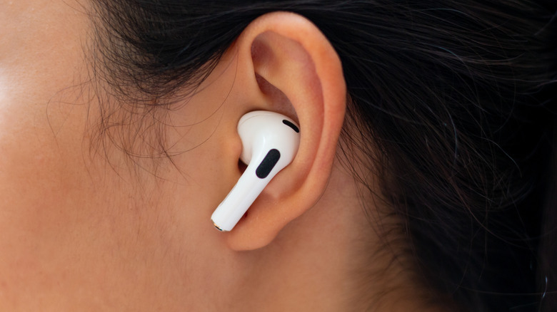 A closeup of a white Apple AirPods earbud inside someone with black hair's left ear