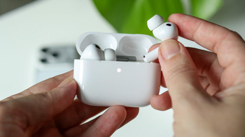 Humans hands hold the white charging case for the AirPods Pro, the user also has the left AirPods in their right hand