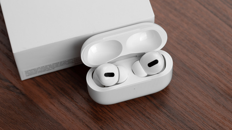 A pair of white Apple AirPods Pro sitting in their charging case on a desk next to their packaging