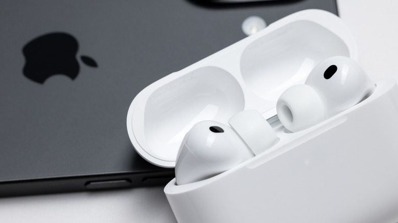 The AirPods Pro inside their white charging case sitting on top of a black iPhone, both objects are sitting on a white background
