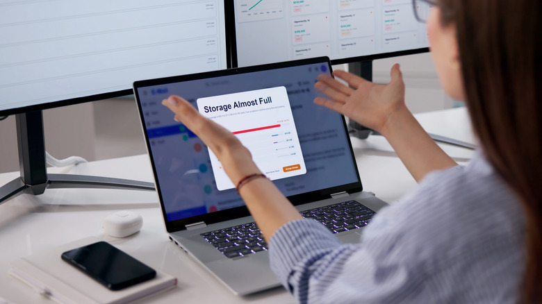 A woman looking at a storage alert on her laptop, holding her hands out in frustration and disbelief