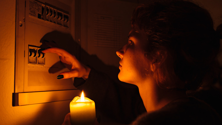 A person holding a candle while checking a circuit breaker during a blackout