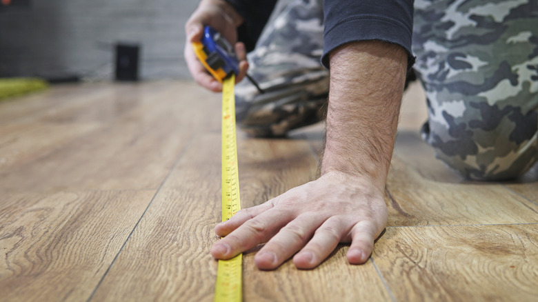 A person holding a measuring tape down on a wooden floor