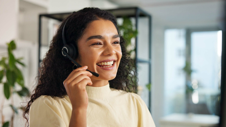 A person smiling while wearing a headphone, holding its mic and talking into it