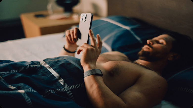 A man lying in bed on his phone wearing a Whoop band