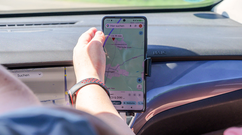 A person touching a smartphone mounted on the car dashboard that's running Google Maps