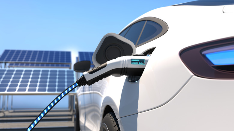 Electric vehicle plugged in for charging with solar panels in the background