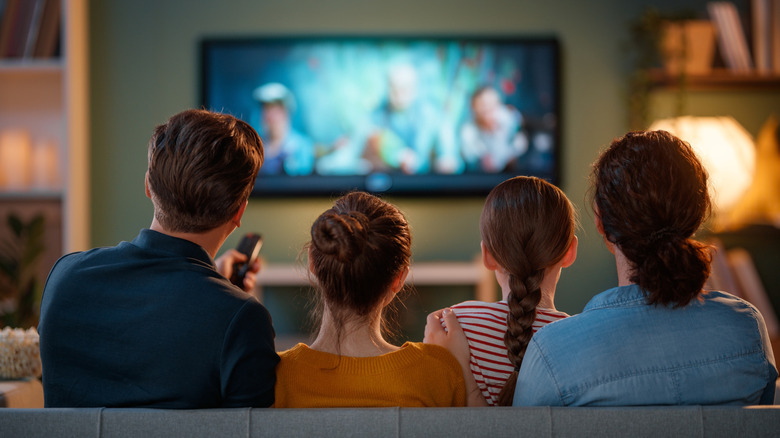 A family seated in front of a TV in a living room.