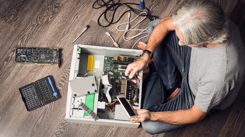 Person repairing a desktop PC with tools and components spread across the floor.