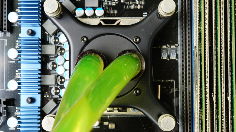 Custom PC liquid cooling block with green tubes connected to a motherboard.
