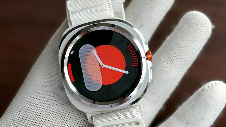 A human hand wearing a clean, white glove holds a Samsung Galaxy Ultra Watch with a white band, the device is displaying the time
