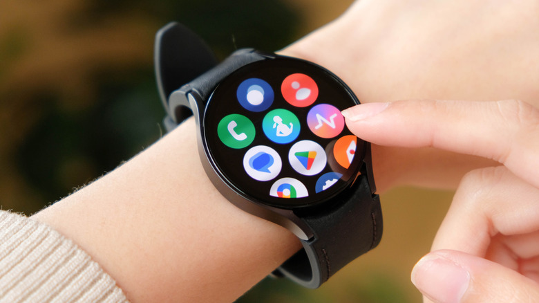 A closeup of an individual wearing a Samsung Galaxy Watch 6 on their right wrist as they prepare to touch the screen with the index finger on their left hand