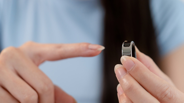 A woman holding a smart ring in one hand and holding out her finger to put it on the other.