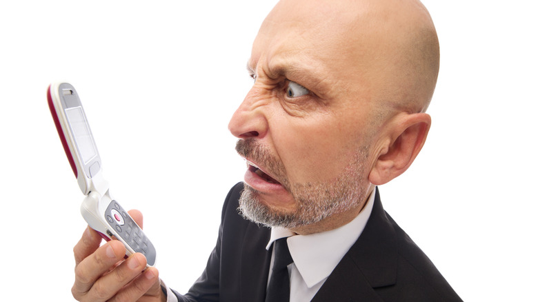 A man stares in frustration at his flip phone.