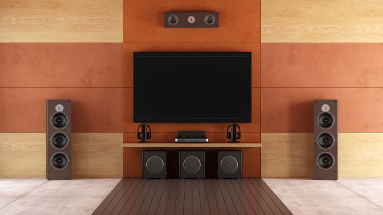 A modern sound system sits near a TV hanging on a wall, the room has an interesting design that creates a cross pattern
