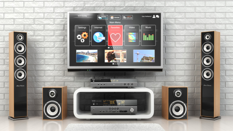 A home audio system featuring speakers encased in a light wood finish with black faceplates sits around a flatscreen television hanging on a white brick wall
