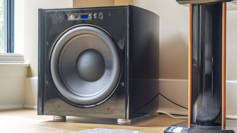A black subwoofer sits on the floor of a home that is mostly white