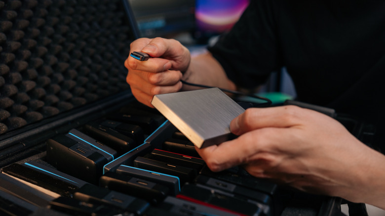 Closeup of technician hands holding portable SSD hard drive and USB cable.