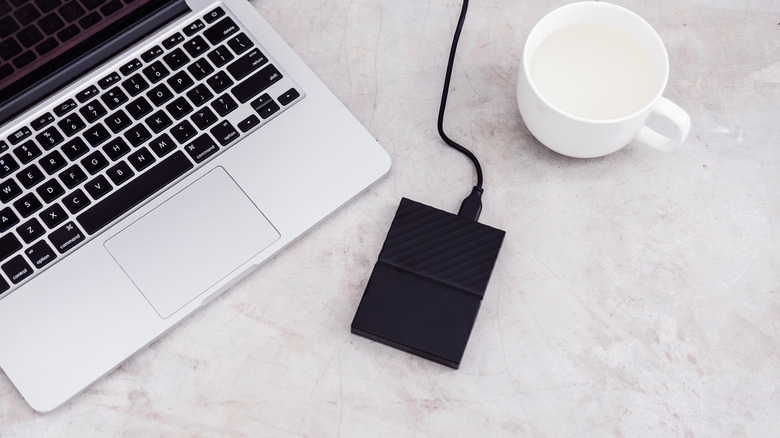 External hard drive connected to the laptop and white mug on grey concrete background