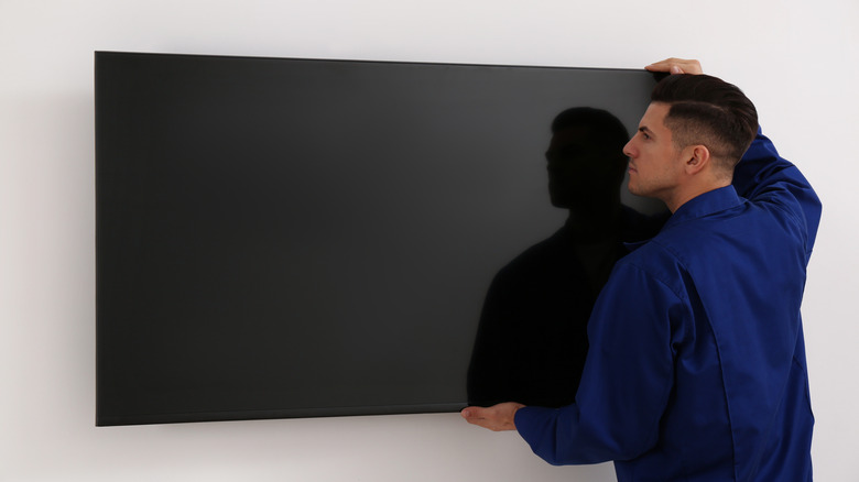 Technician mounting a large flat-screen TV on a white wall.