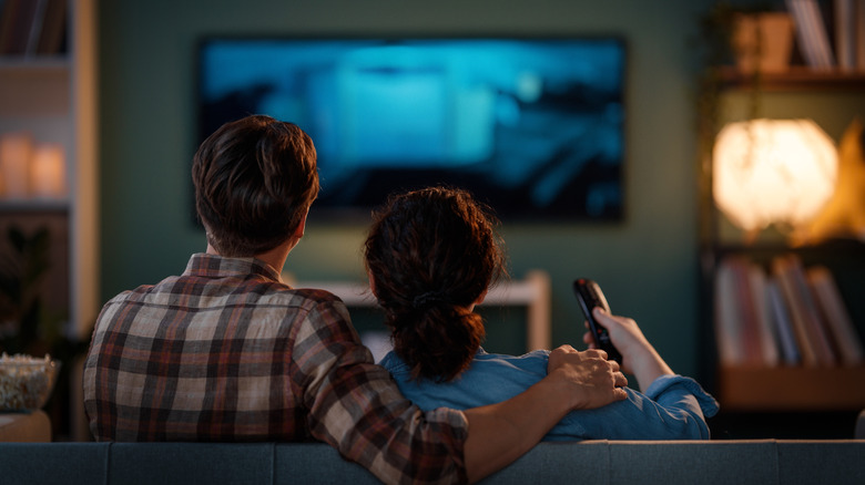 Two people sitting on a couch watching TV in a softly lit living room.