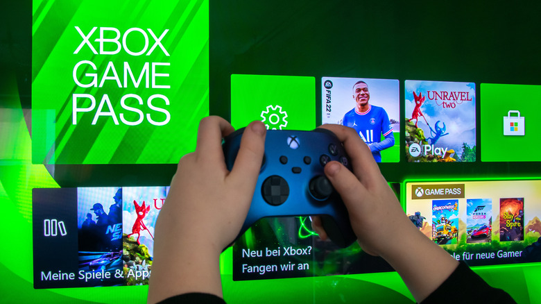 Person using an Xbox controller in front of the Xbox Game Pass menu on a TV.