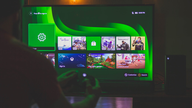 Person playing Xbox with the console home menu displayed on a TV.