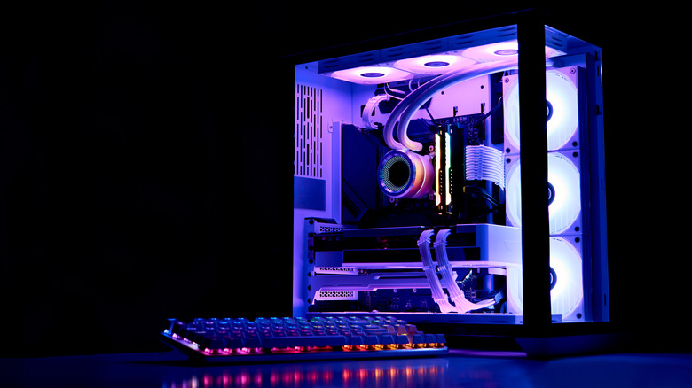 A gaming PC with purple internal lights next to an RGB keyboard