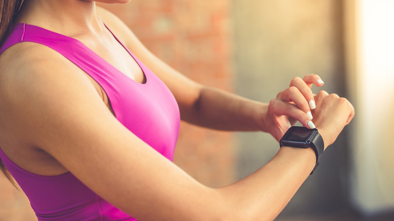 A woman with her finger holding down the button on a Fitbit smartwatch.