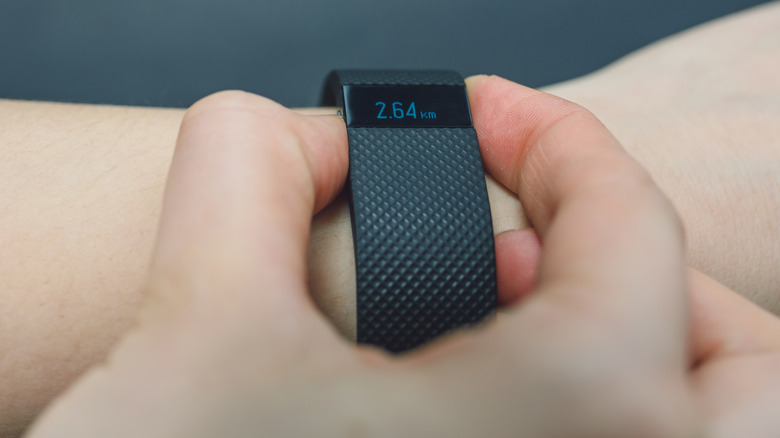 A hand with two fingers on an old Fitbit tracker holding down buttons.