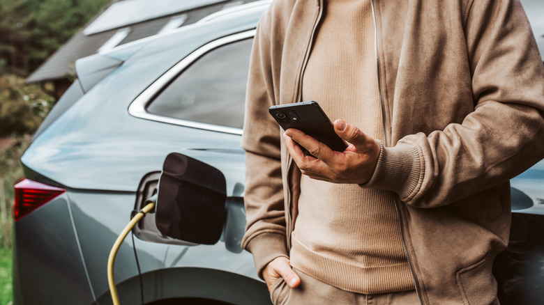 Man checking phone while charging electric car