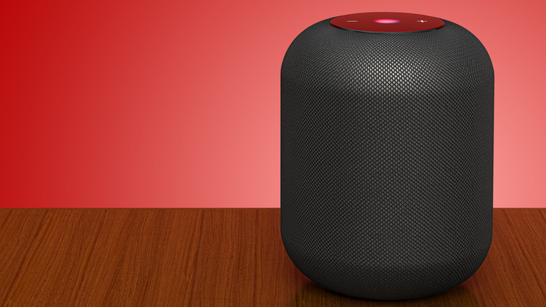 A black Apple HomePod speaker set against a red backdrop.