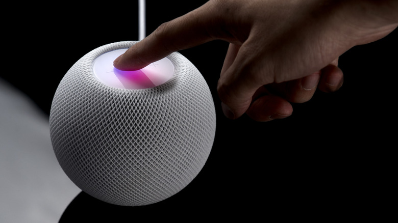 A hand presses down on the top of the HomePod