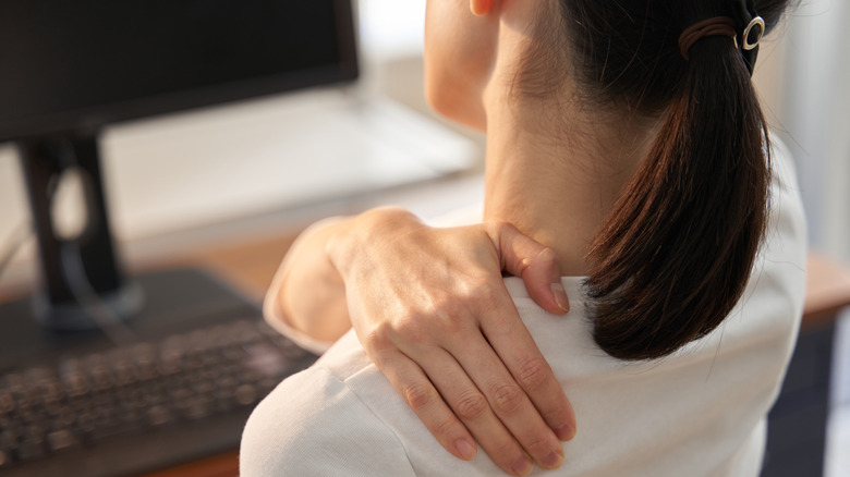 woman in front of desktop with monitor and keyboard, struggling from neck/shoulder pain
