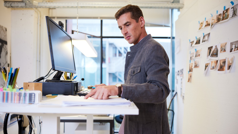 man using standing desk, pointing at papers on the desktop