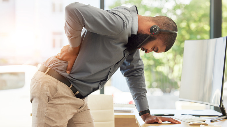 man in call center with headset on struggling with back pain