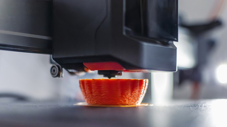 3D printer nozzle depositing molten filament while fabricating a small object.