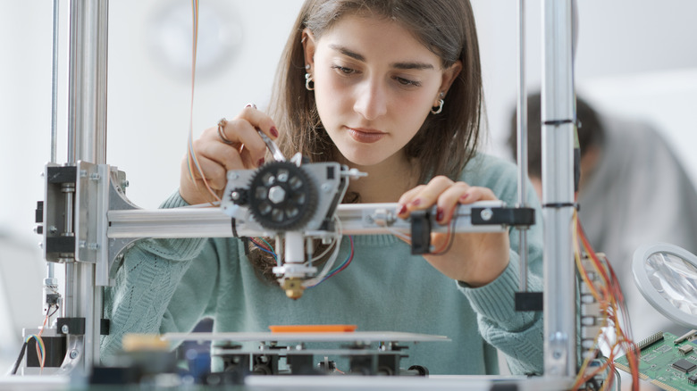 Person adjusting a desktop 3D printer while preparing it for a print job.
