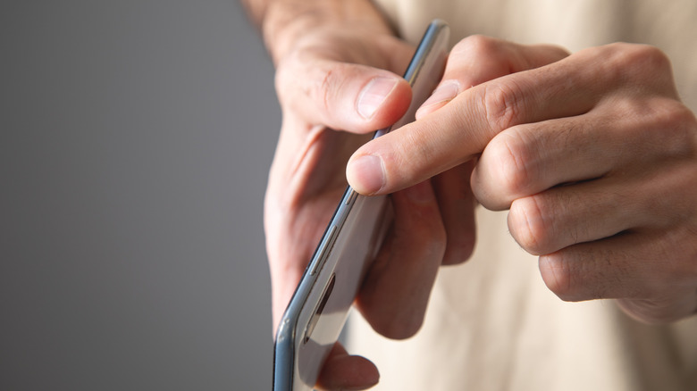 person pressing the power button on a smartphone with one hand while holding it in another