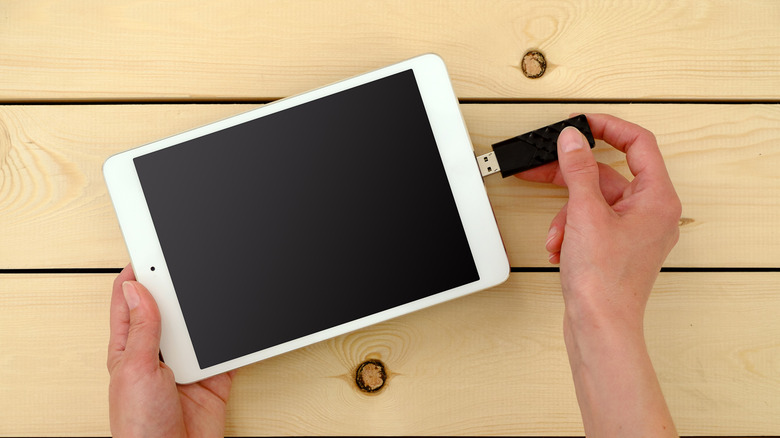 A person connecting a flash drive into a white tablet over a light wooden surface