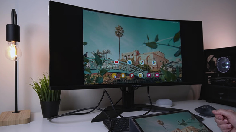 An Android tablet placed on a workstation with its display mirrored to an ultra-wide monitor