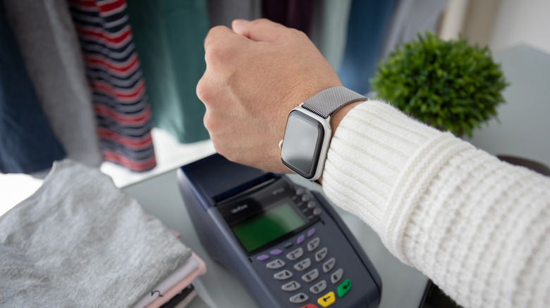 A person holding out their smartwatch to a card read to pay via NFC