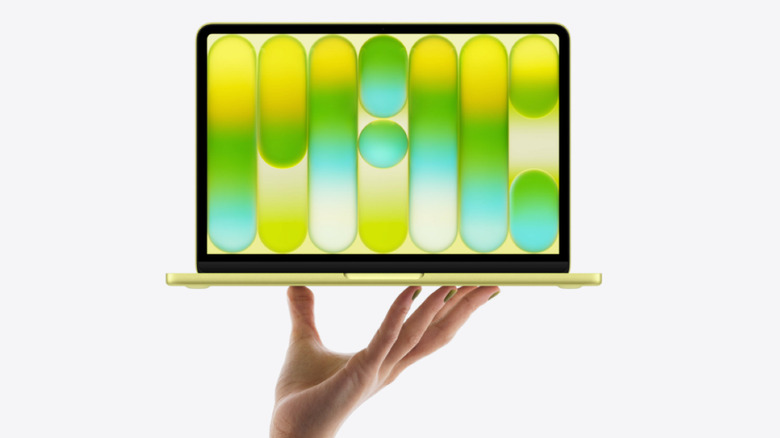 An open yellow MacBook Neo being held up in one hand on a white background