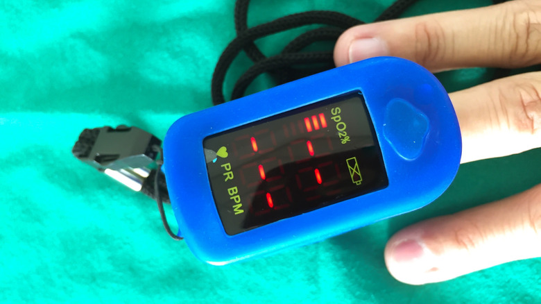 Blue pulse oximiter on finger measuring heart rate and blood oxygenation