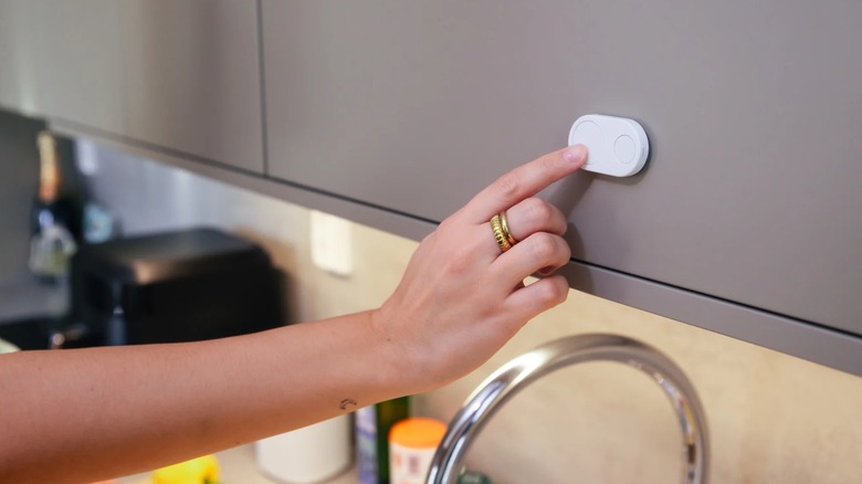 Hand pushing Flic Duo mounted on kitchen cabinet