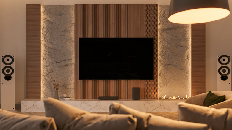 A modern living room showing a mounted TV with multiple speakers and audio devices around it