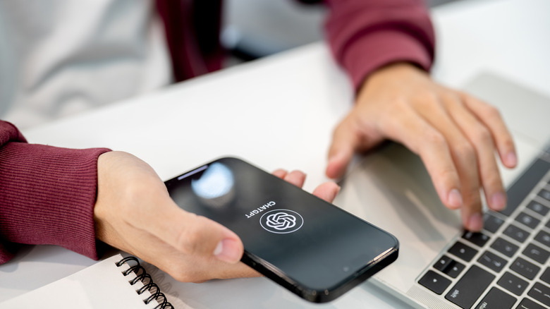 person with a laptop and holding a phone with the chatgpt app open