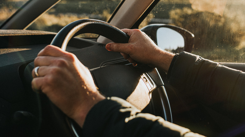 A person's hands gripping a steering wheel as they drive.