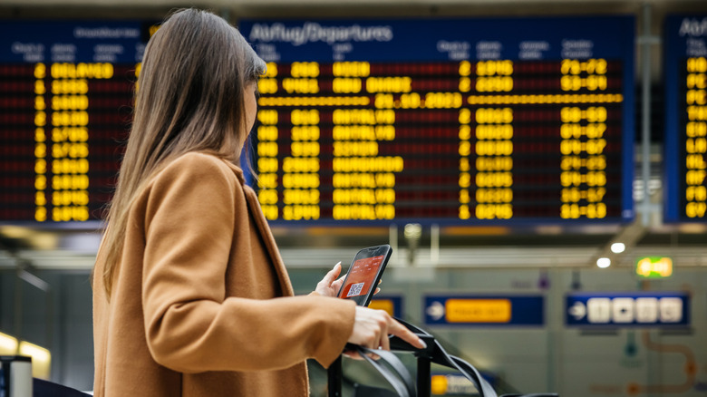 woman looking at her phone at an airport with one hand on her bags