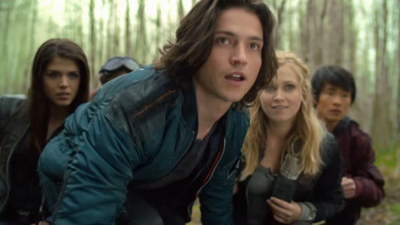 Finn, Clarke Griffin and Bellamy Blake crouch with fellow survivors while scouting the forest in The 100.